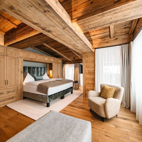 Ihre Unterkunft in St. Christoph am Arlberg: Bilder Gemütliches Schlafzimmer mit Holzbalken, Bett und Sessel neben großen Fenstern