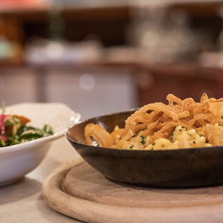 Ihre Unterkunft in St. Christoph am Arlberg: Bilder Käsespätzle mit Röstzwiebeln in einer Pfanne und Salat in weißer Schale
