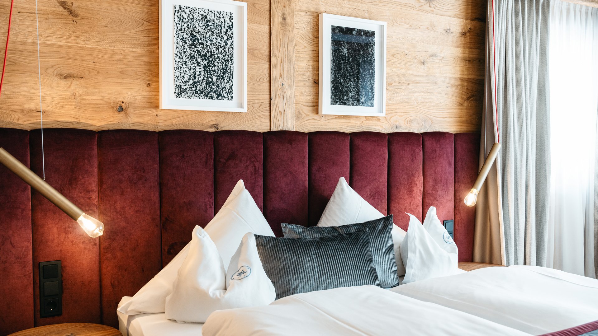 Zum Pressebereich des Hotel Maiensee Modernes Schlafzimmer mit rotem Kopfteil, weißen Kissen und Holzverkleidung