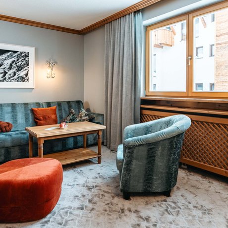 Ihre Unterkunft in St. Christoph am Arlberg: Bilder Gemütliche Sitzecke mit Sofa, Sesseln, rotem Hocker und Holzfenster