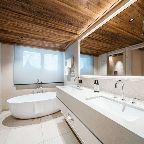 Ihre Unterkunft in St. Christoph am Arlberg: Bilder Moderne Badezimmerszene mit Badewanne, Doppelwaschbecken und Holzdecke.
