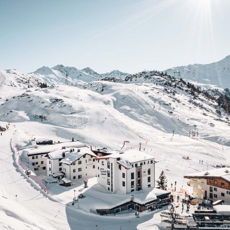 Ihre Unterkunft in St. Christoph am Arlberg: Bilder Schneebedeckte Berglandschaft mit Hotels und Skifahrern an sonnigem Wintertag