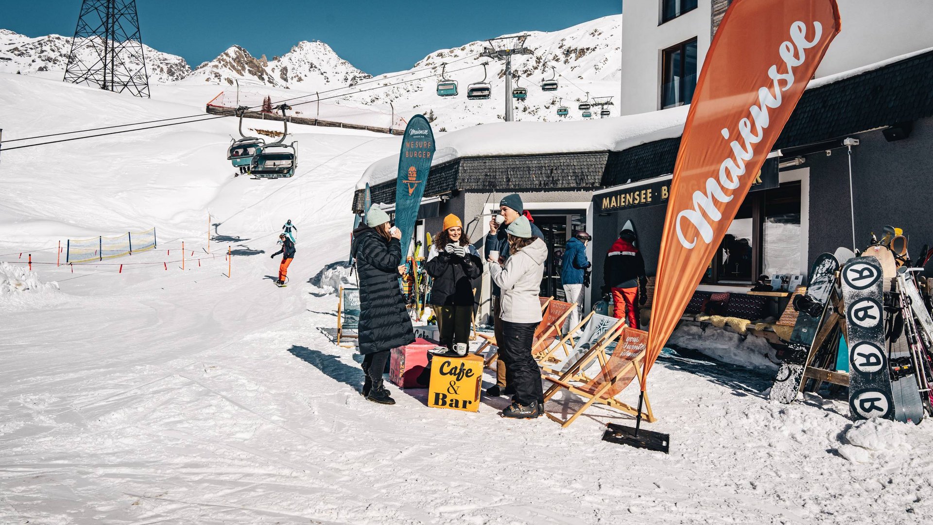 Maiensee, Ihr Hotel in Sankt Christoph: Kulinarik Menschen genießen warme Getränke vor Café und Bar in verschneiter Berglandschaft