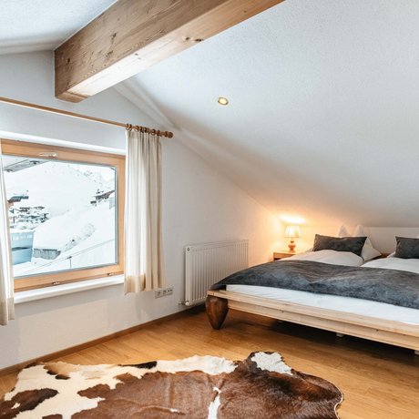 Ihre Unterkunft in St. Christoph am Arlberg: Bilder Gemütliches Schlafzimmer mit Holzboden, Fenster mit Bergblick und Tierfellteppich