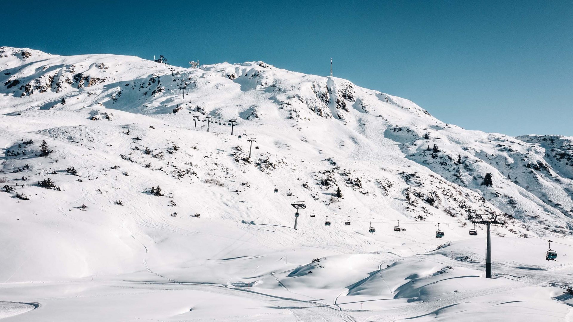Arlberg: Ihr Hotel an der Piste Verschneiter Berg mit Sessellift unter klarem Himmel