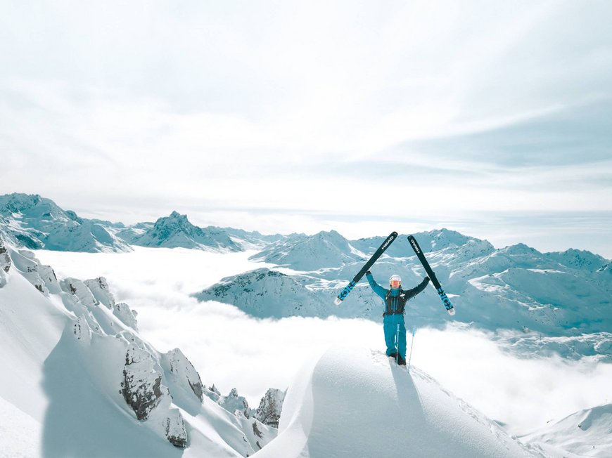 Arlberg: Ihr Hotel an der Piste Skifahrer hebt Ski auf schneebedecktem Berg mit Alpen im Hintergrund