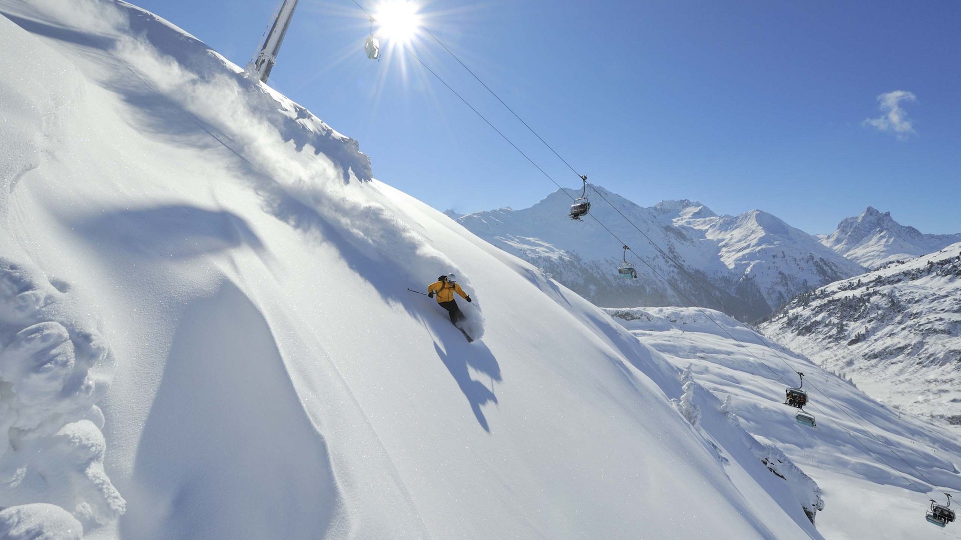 Arlberg: Ihr Hotel an der Piste Skifahrer in gelber Jacke fährt im Tiefschnee an sonnigem Tag in den Bergen