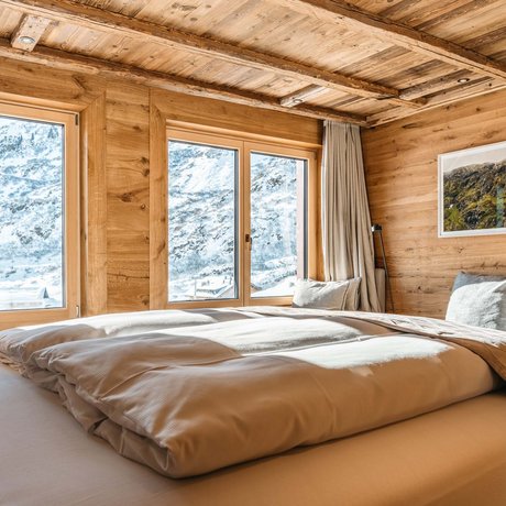 Ihre Unterkunft in St. Christoph am Arlberg: Bilder Gemütliches Schlafzimmer mit Holzwänden und Blick auf verschneite Berge