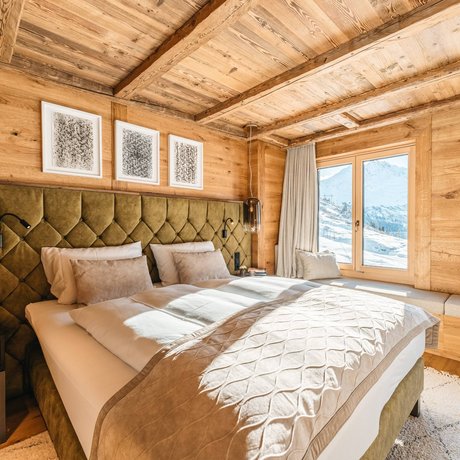 Ihre Unterkunft in St. Christoph am Arlberg: Bilder Gemütliches Schlafzimmer mit Holzwänden und Bergblick durch große Fenster