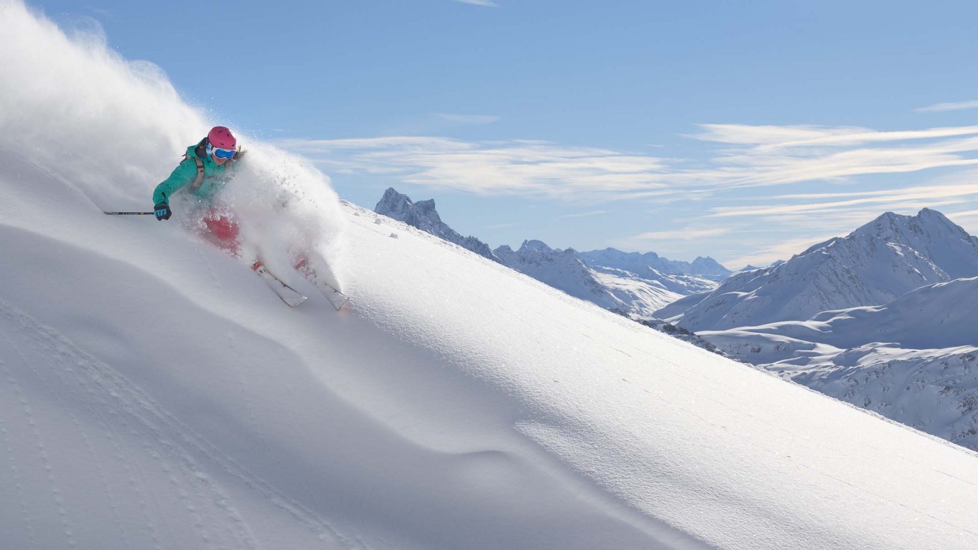 Arlberg: Ihr Hotel an der Piste Skifahrer fährt durch frischen Pulverschnee an einem sonnigen Berghang