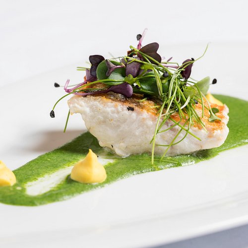 Genuss pur im 4-Sterne-Hotel in St. Anton Gebratenes Fischfilet mit grüner Sauce, Kräutern und zwei kleinen Dips auf weißem Teller