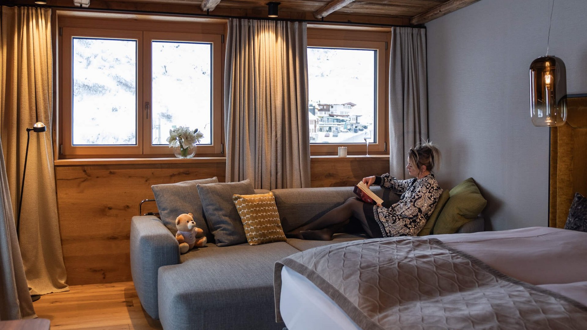 Buchen Sie Ihren Urlaub im Maiensee, Ihrem Hotel am Arlberg Frau liest auf Sofa im gemütlichen Zimmer mit Holzbalkendecke und Alpenblick
