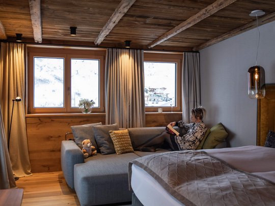 Hotel Maiensee: your hotel in St. Christoph Woman reading on sofa in cozy room with wooden beams and Alpine view