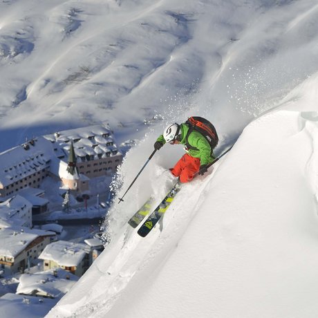 Ihre Unterkunft in St. Christoph am Arlberg: Bilder Skifahrer fährt steilen verschneiten Hang mit Bergdorf im Hintergrund hinab