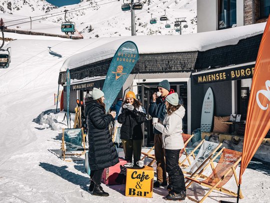 Premium burgers at the ski hotel near St. Anton am Arlberg Group drinking coffee outside mountain café in snow with ski lift in background