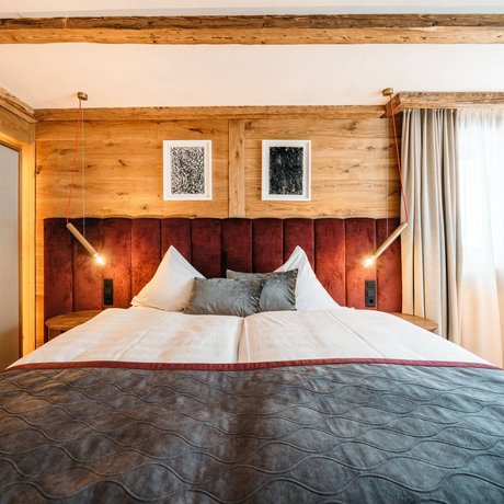 Ihre Unterkunft in St. Christoph am Arlberg: Bilder Gemütliches Schlafzimmer mit Holzdecke, rotem Kopfteil und modernem Licht