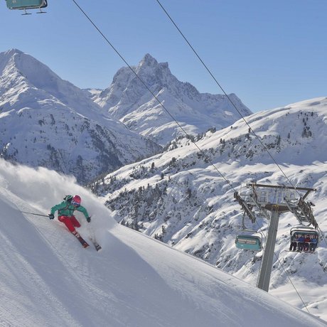 Ihre Unterkunft in St. Christoph am Arlberg: Bilder Skifahrer fährt steil im Pulverschnee in den verschneiten Alpen neben Sessellift