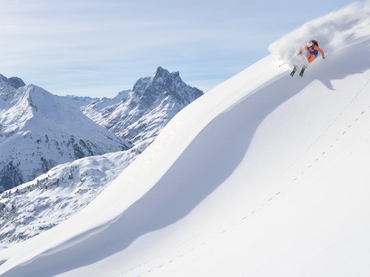 Arlberg: Ihr Hotel an der Piste Skifahrer fährt auf steilem schneebedecktem Hang in den Alpen