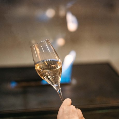 Ihre Unterkunft in St. Christoph am Arlberg: Bilder Hand hält ein Weinglas mit weißem Wein vor unscharfem Hintergrund