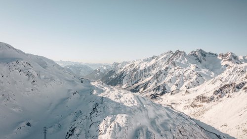 Skiurlaub am Arlberg: Anfrage Verschneite Alpenberge unter klarem Himmel mit Sicht auf ein Tal und Straße