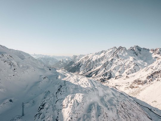 Arlberg: Ihr Hotel an der Piste Verschneite Alpenberge unter klarem Himmel mit Sicht auf ein Tal und Straße