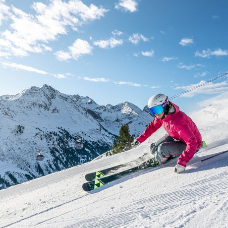 Ihre Unterkunft in St. Christoph am Arlberg: Bilder Skifahrer in roter Jacke fährt schnell auf schneebedecktem Berg mit Seilbahn im Hintergrund