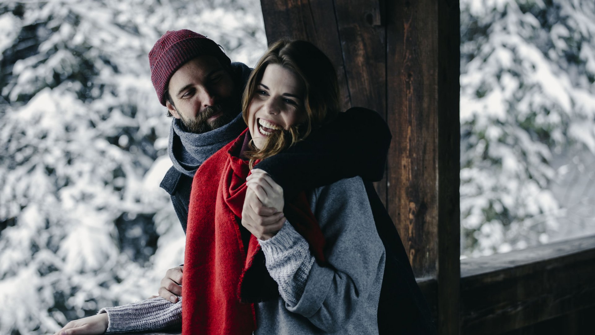 Excursion tips for your holiday near St. Anton Couple hugging on balcony with snow and pine trees in the background