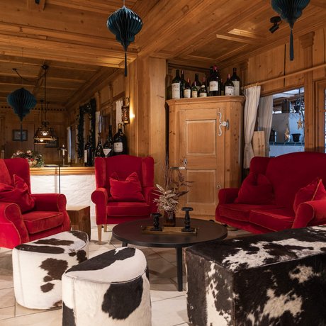 Ihre Unterkunft in St. Christoph am Arlberg: Bilder Rustikaler Wohnbereich mit roten Sesseln und Kuhfellhockern in Holzhütte