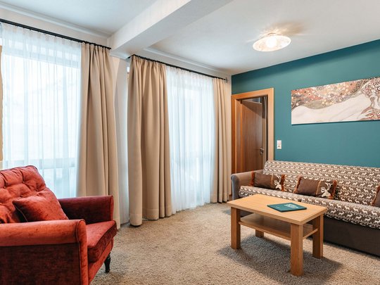 Hotel Maiensee: your hotel in St. Christoph Cozy living room with red armchair, sofa, wooden table, and artwork on wall