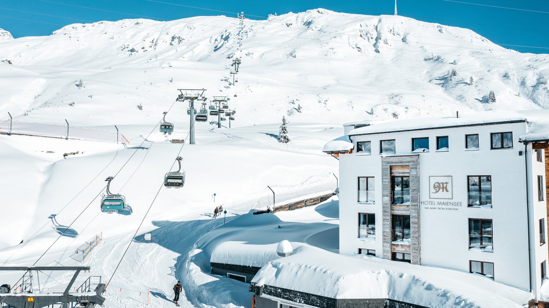 Zum Pressebereich des Hotel Maiensee Winteransicht eines Skilifts und verschneiter Berge mit Hotel Maiensee