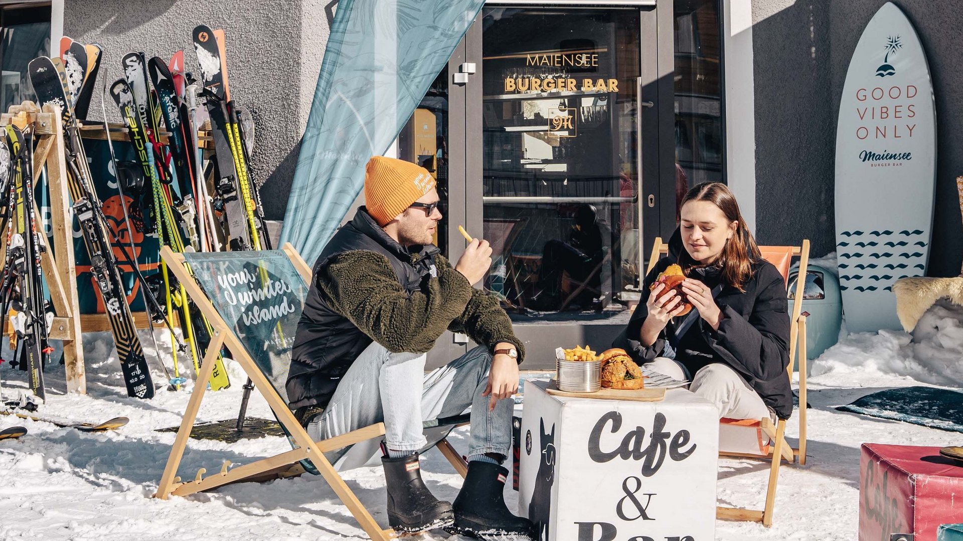 Maiensee, Ihr Hotel in Sankt Christoph: Kulinarik Zwei Menschen essen draußen Burger in einem Café im Schnee neben Skiern
