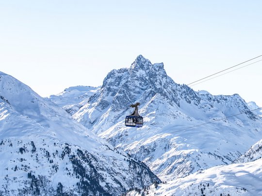 Arlberg: Ihr Hotel an der Piste Seilbahn über schneebedeckte Berge mit klarem Himmel